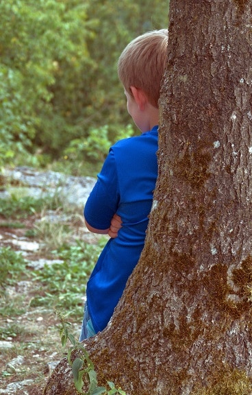 A child sulking behind a tree
