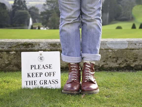 Someone standing next to a "Please Keep Off The Grass" sign