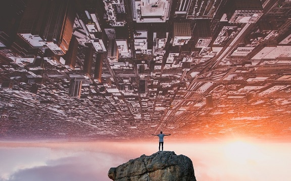 Man standing on rock underneath overturned city